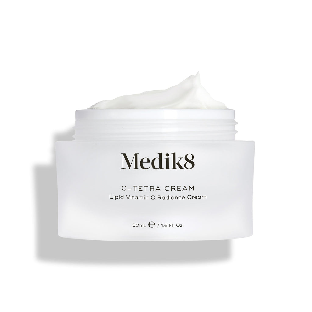 Otevřená dóza Medik8 C-Tetra Cream je zobrazena na čistém bílém pozadí s jemnými stíny.

Bílá matná skleněná dóza nese logo Medik8 a je označena jako C-TETRA CREAM Lipid Vitamin C Radiance Cream ve velikosti 50 ml. Na vrchu je viditelná bohatá vrstva bílé krémové textury, která zvýrazňuje její hydratační konzistenci.