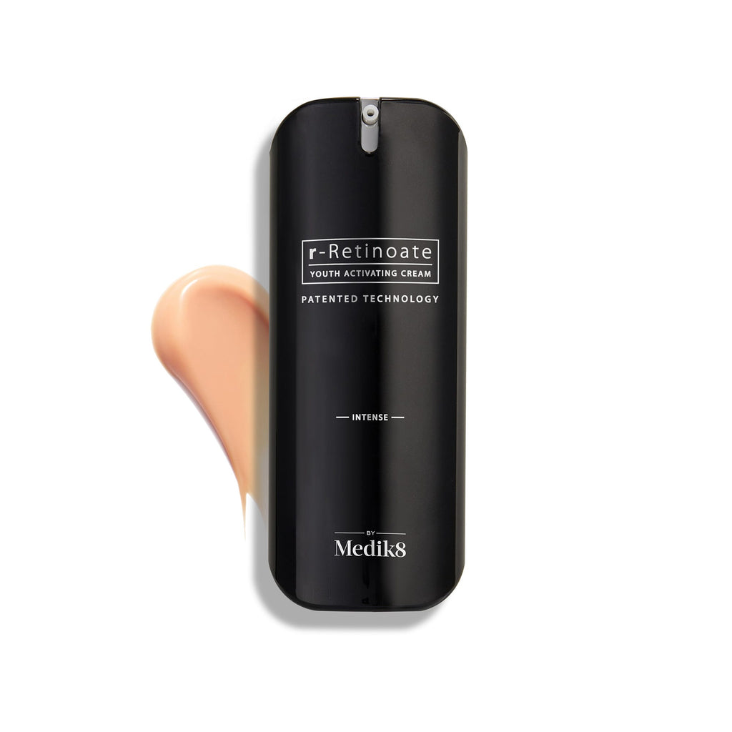 Lahvička Medik8 r-Retinoate Intense Youth Activating Cream je zobrazena na bílém pozadí spolu se vzorkem broskvově zbarvené krémové textury viditelným za ní.