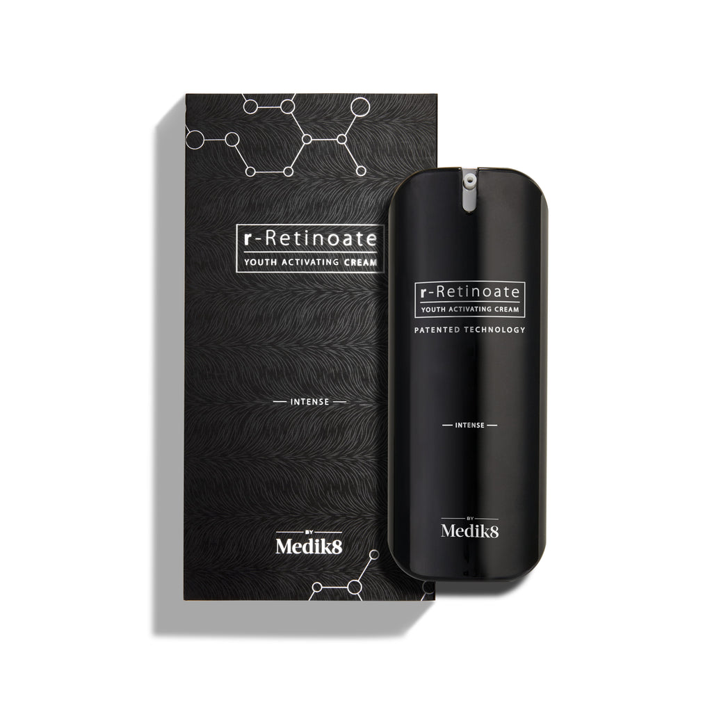Lahvička Medik8 r-Retinoate Intense Youth Activating Cream stojí vedle své černé vnější krabičky, která obsahuje bílé grafiky chemických hexagonálních struktur a texturovaný vlnitý vzor.