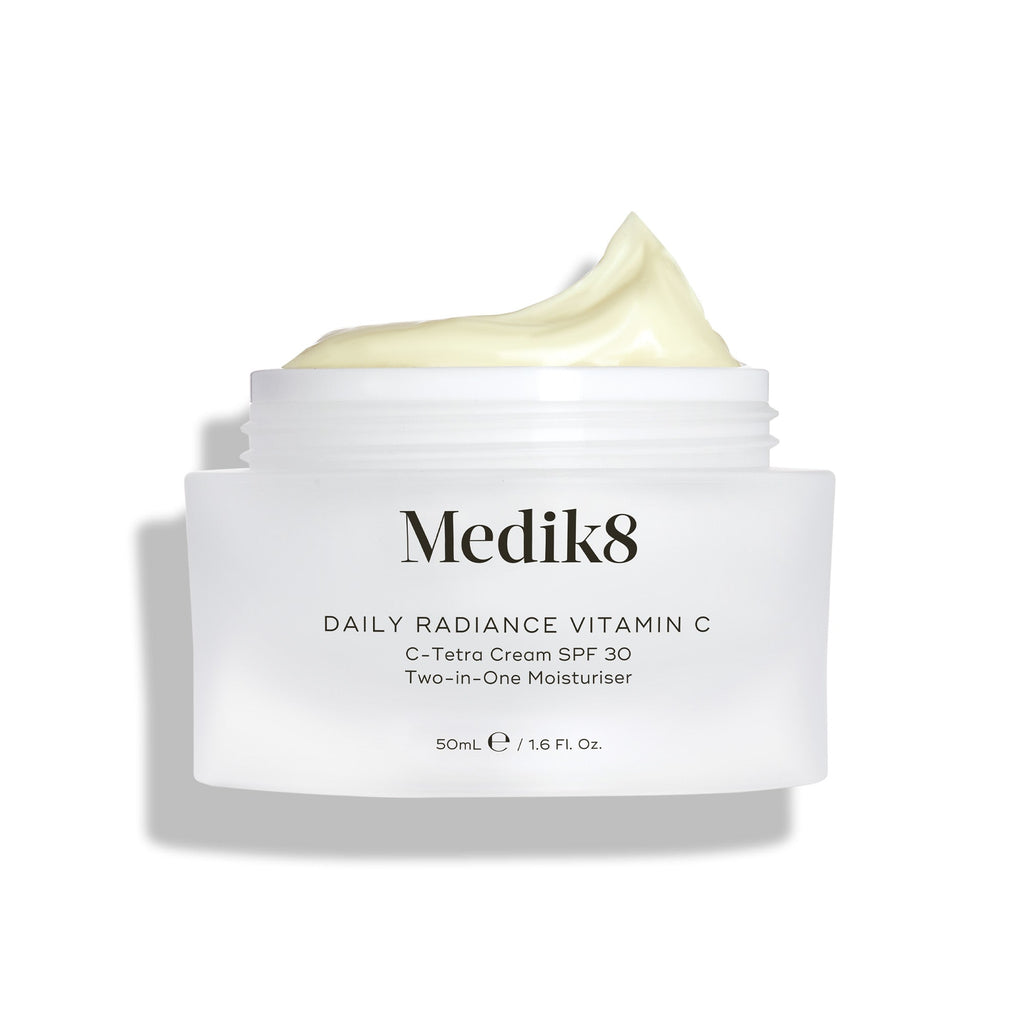 Otevřený skleněný kelímek Medik8 Daily Radiance Vitamin C je zobrazen s bohatou špičkou světle žlutého krému nahoře. Text označuje produkt jako 50ml C-Tetra krém SPF 30 – dvoukrokový (2-in-1) hydratační krém.