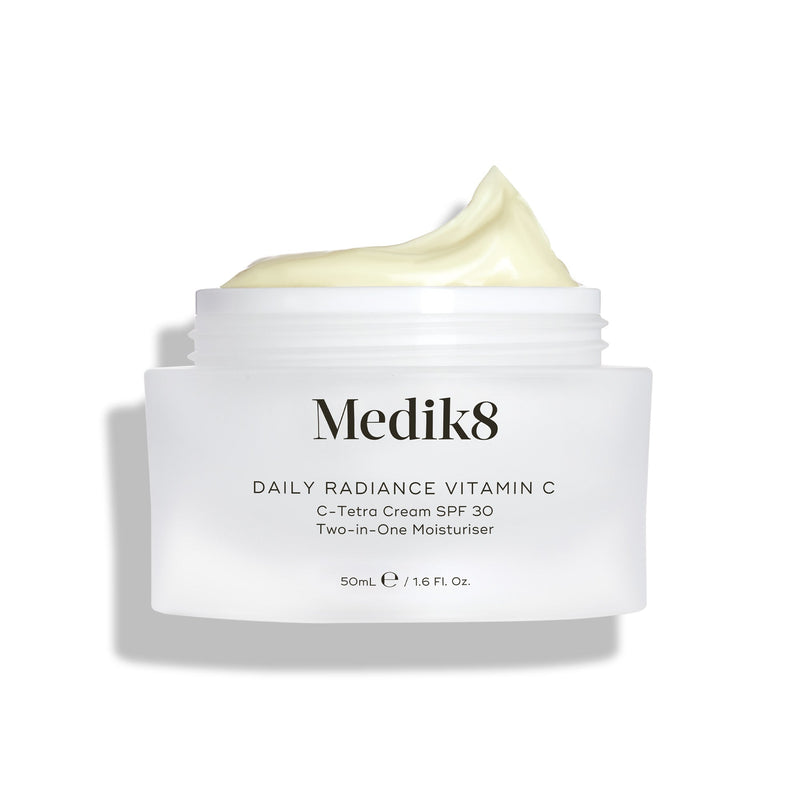 Otevřený skleněný kelímek Medik8 Daily Radiance Vitamin C je zobrazen s bohatou špičkou světle žlutého krému nahoře. Text označuje produkt jako 50ml C-Tetra krém SPF 30 – dvoukrokový (2-in-1) hydratační krém.