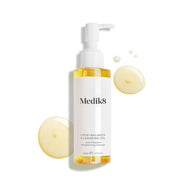 Lahvička Medik8 Lipid-Balance Cleansing Oil stojí na bílém pozadí. Zlaté kapky oleje ji obklopují a zdůrazňují její bohatou, tekutou texturu.