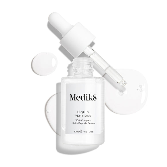 Průhledná skleněná lahvička séra Liquid Peptides je zobrazena s vyjmutým kapátkem položeným vedle ní. Kolem jsou viditelné kapky séra, které zdůrazňují jeho texturu.-18