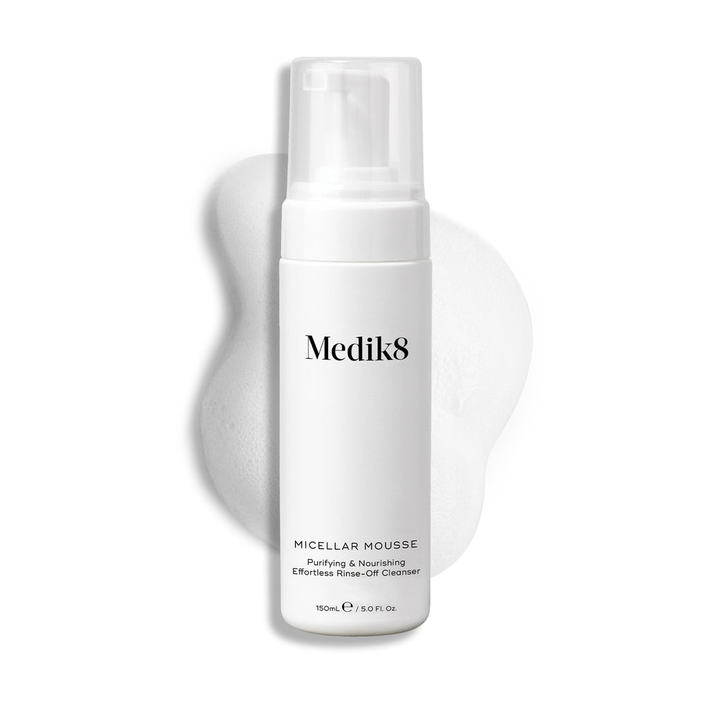 Pumpičková lahvička Medik8 Micellar Mousse zobrazená na bílém pozadí s rozmazanou stopou bílé pěny za ní, která zvýrazňuje texturu produktu.