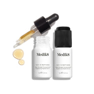 Dvě malé bílé lahvičky séra Oxy-R Peptides jsou vystaveny. V blízkosti leží černý kapátkový aplikátor a na bílém povrchu jsou viditelné dvě kapky žlutého séra.