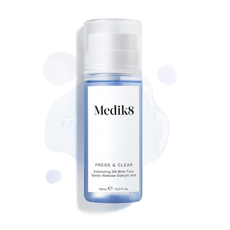 Láhev Medik8 Press & Clear (150 ml) na bílém pozadí, kolem ní jsou rozstříknuté kapky modrého tonika. Text zdůrazňuje složení  Exfoliating 2% BHA Tonic.