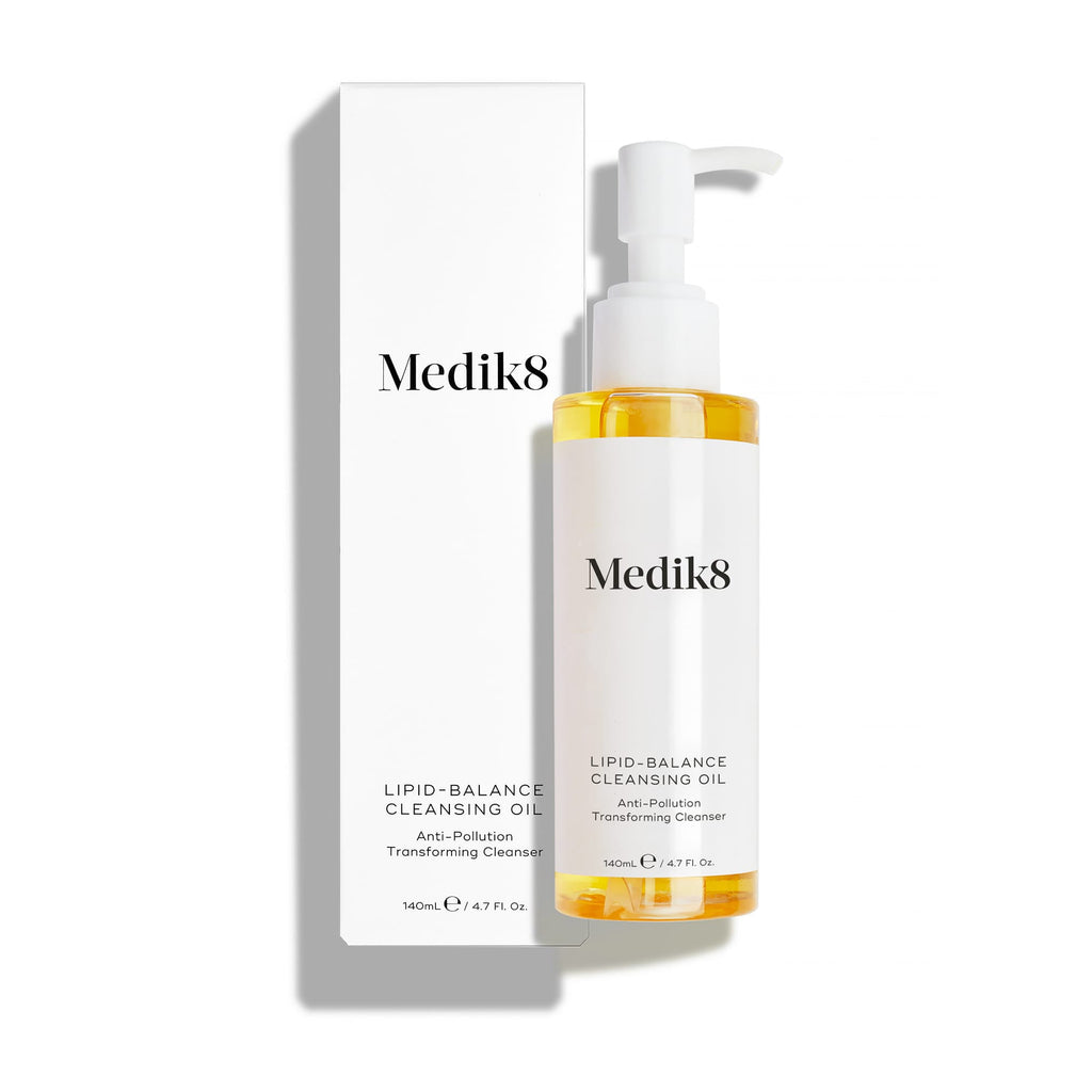 Lahvička Medik8 Lipid-Balance Cleansing Oil stojí vedle své bílé krabičky. Text zvýrazňuje složení „Anti-Pollution Transforming Cleanser“ (transformační čisticí olej proti znečištění) a objem 140 ml.