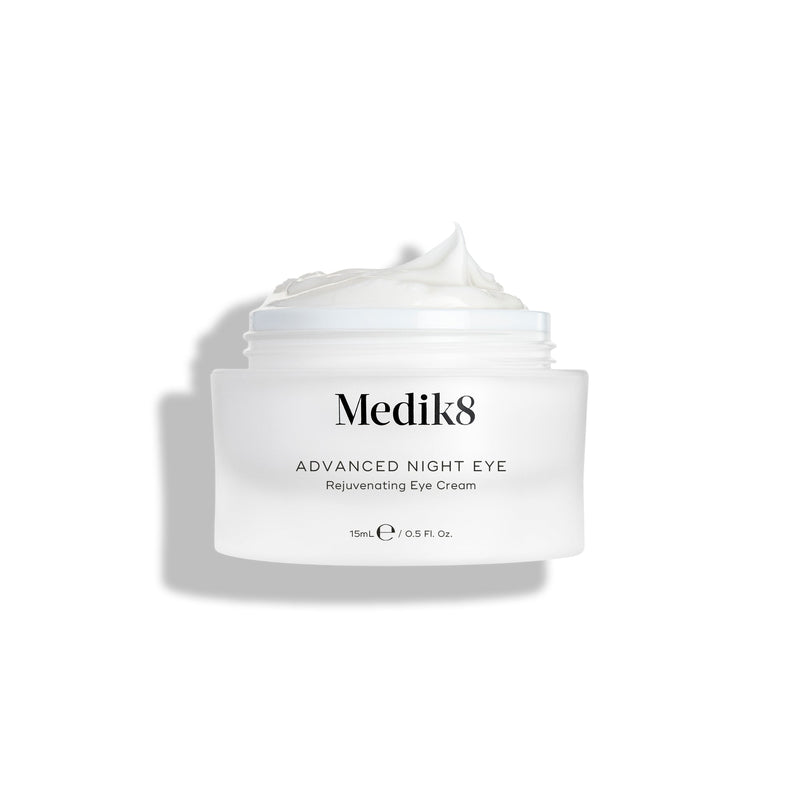 Kelímek krému Medik8 Advanced Night Eye stojí na bílém pozadí s odklopeným víčkem. Uvnitř je viditelný bohatý bílý krém, který zdůrazňuje jeho texturu.