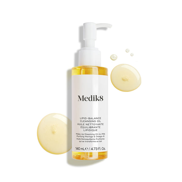 Lahvička čisticího oleje Medik8 Lipid-Balance Cleansing Oil stojí na bílém pozadí. Kolem lahvičky jsou zobrazeny zlatavé kapky oleje, které zdůrazňují jeho bohatou tekutou texturu.-3