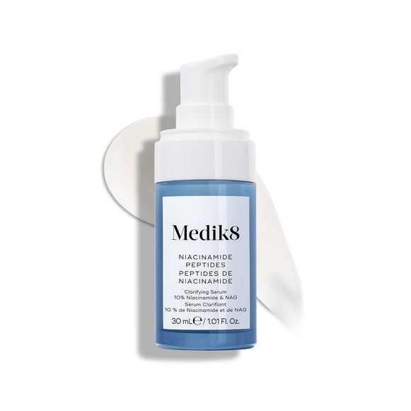 Lahvička séra Medik8 Niacinamide Peptides s bílým pumpičkovým uzávěrem je položena na bílém povrchu s tahem bílého séra za ní.-11