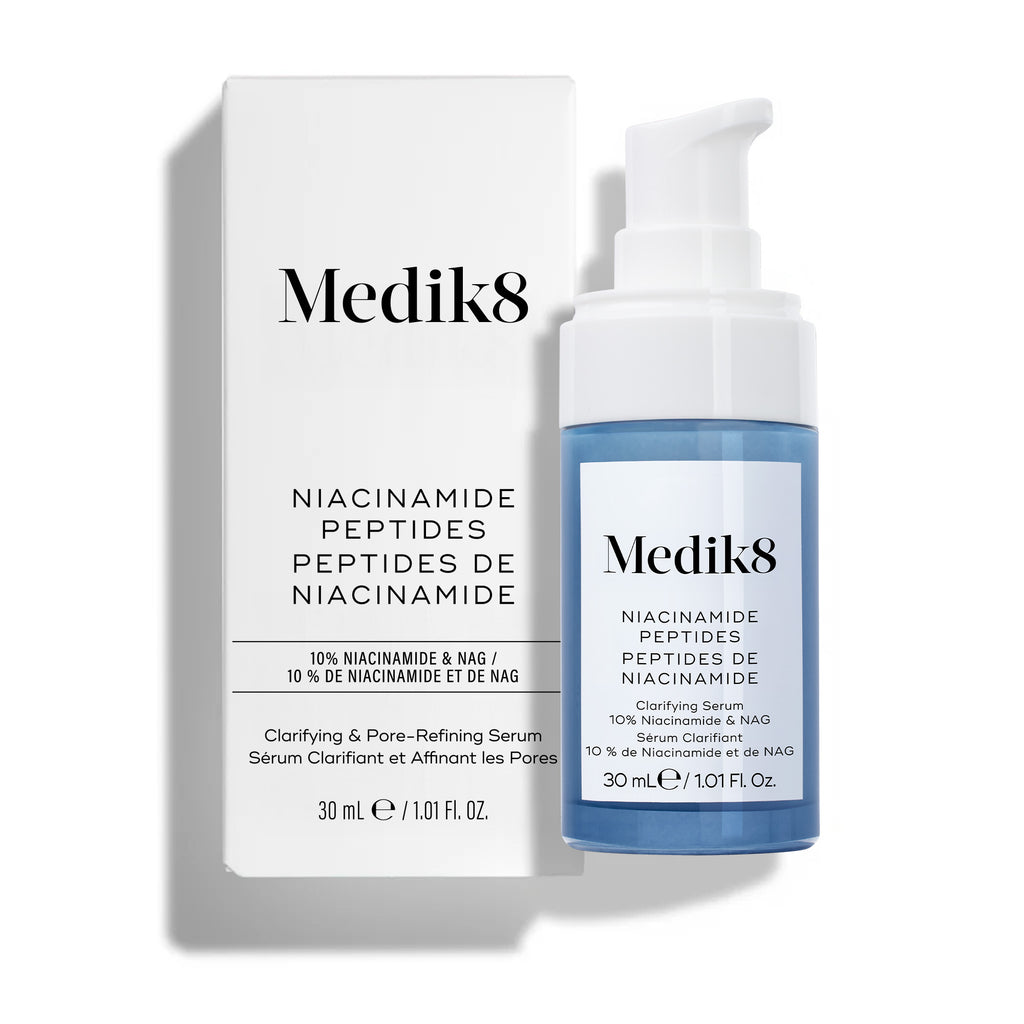 Lahvička čisticího séra Medik8 Niacinamide Peptides s bílou pumpičkou stojí vzpřímeně vedle své bílé produktové krabičky na čistém bílém pozadí.