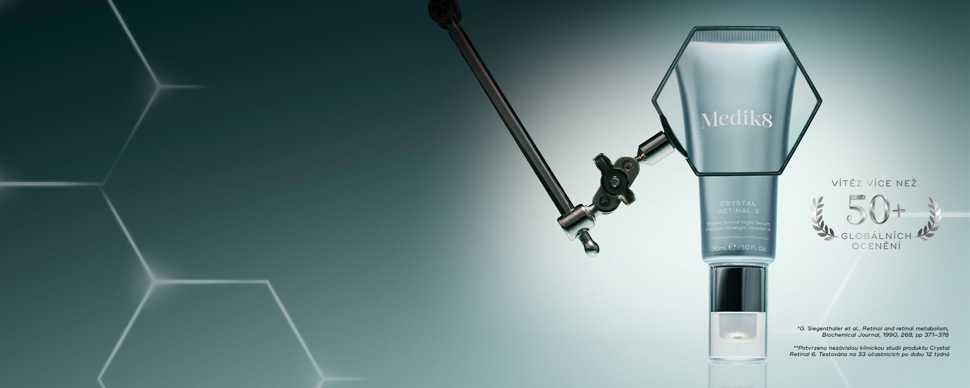 Banner na tmavě námořnicky modrém pozadí. Na pravé straně stojí svisle metalicky stříbrná tuba přípravku Medik8 Crystal Retinal 6 uvnitř jasného, zářivě bílého světelného paprsku ve tvaru kříže. Vlevo od tuby jsou zobrazeny dva stříbrné kovové emblémy: vavřínový věnec s nápisem „VÍTĚZ VÍCE NEŽ 50 MEZINÁRODNÍCH OCENĚNÍ“ a kruhový odznak s nápisem „SVĚTOVÁ NOVINKA • PATENTOVANÁ TECHNOLOGIE“. V pravém dolním rohu je vidět text s drobnými písmeny obsahující informace o produktu.