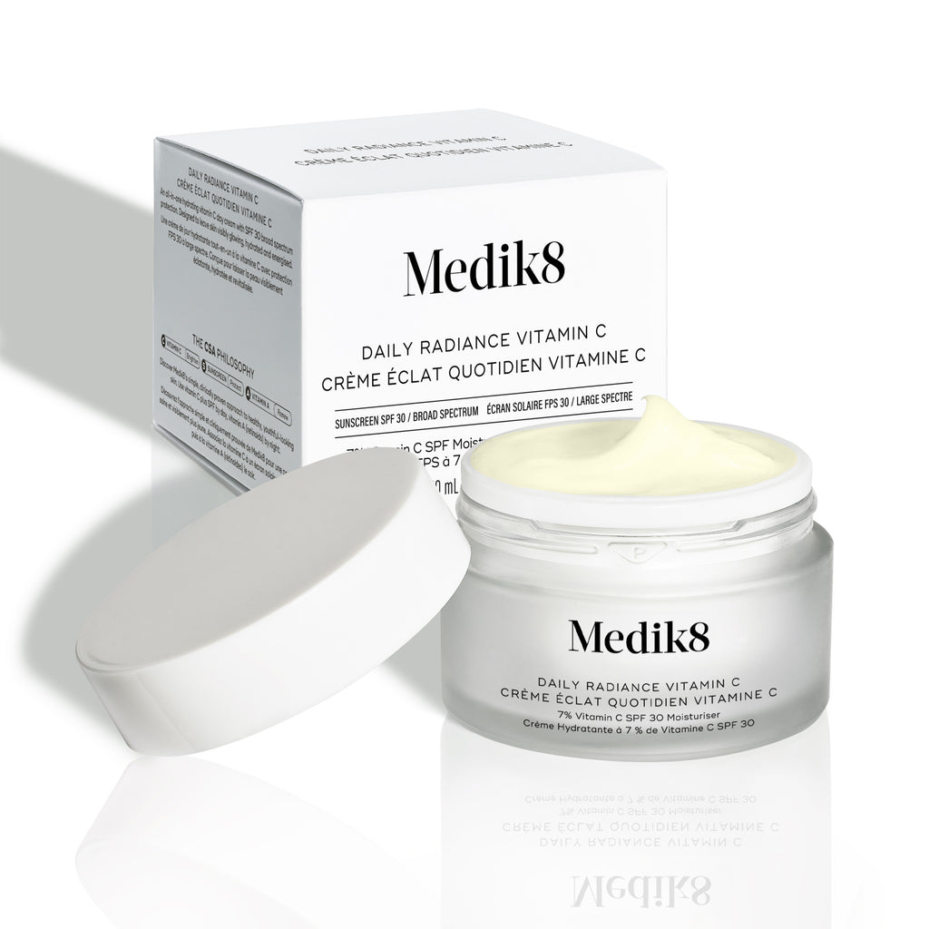 Otevřené víčko krému Medik8 Daily Radiance Vitamin C je zobrazeno před krabičkou produktu, přičemž je viditelná textura krému.